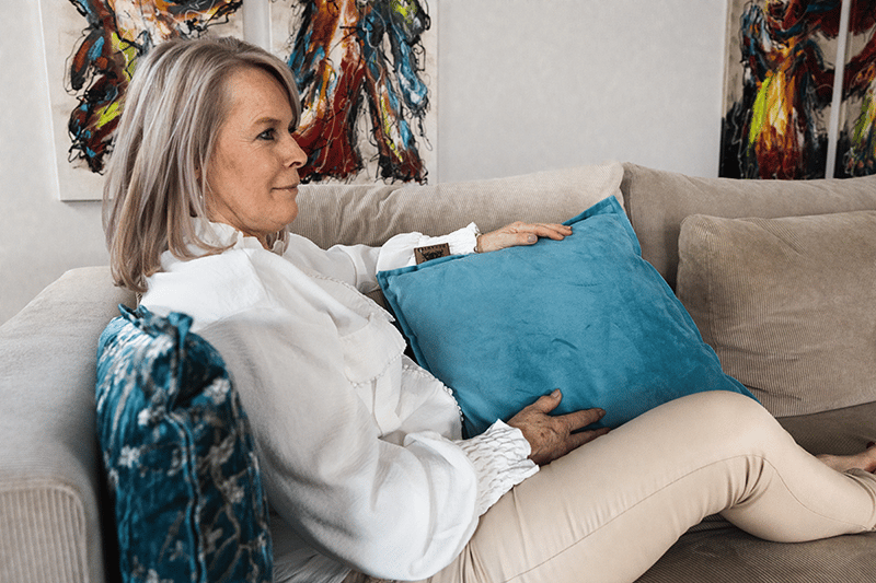 Een blauw warmtekussen wat ervoor zorgt dat de vrouw heerlijk warm blijft op de bank.