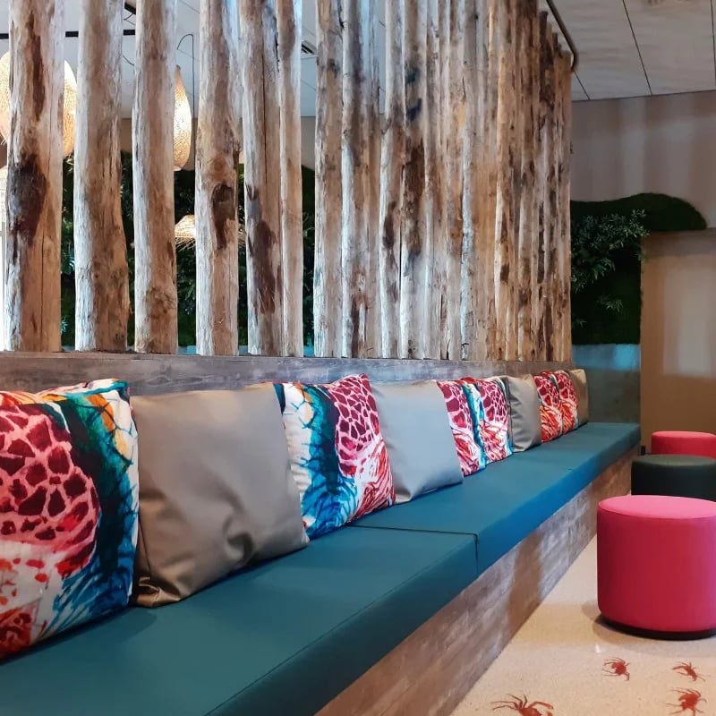 Træbænk med blå siddepuder kombineret med rygpuder med farverigt tryk.