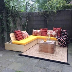 Un banc en bois avec des coussins d'assise jaunes sur mesure avec des coussins décoratifs rouges pour un confort supplémentaire.