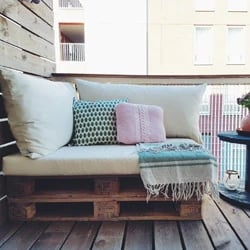 Une palette transformée en siège. Les coussins d'assise sont en vert et les coussins décoratifs en rose et vert.