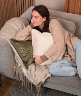 Une femme allongée sur un banc avec différents coussins décoratifs et un coussin chauffant.